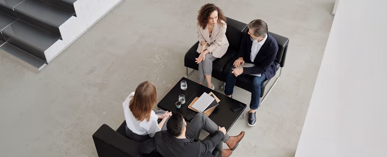 Overhead view of four people in business attire having a meeting on black sofas around a black table.