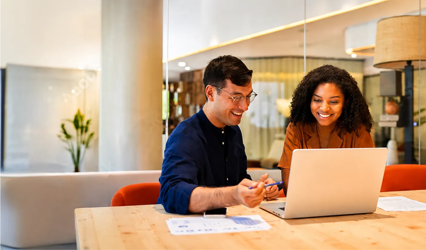 A man and woman sitting at a table looking at a laptop.