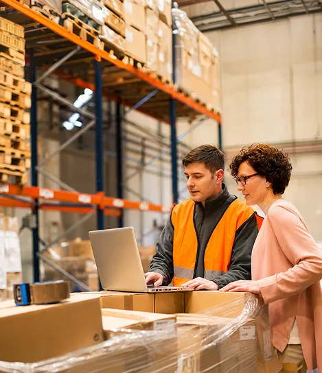 A man and woman working on a laptop in a warehouse.
