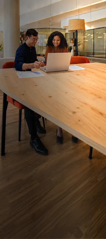 A man and woman sitting at a table with a laptop.
