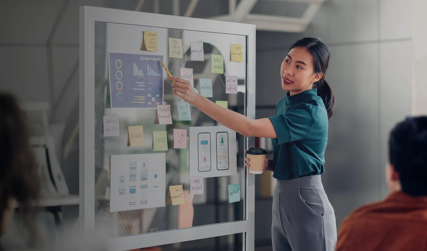 A woman writing on a board with sticky notes on it.