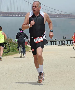 A man running in a marathon with a bridge in the background.