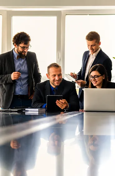 Four professionals smiling and working together with a tablet and laptop in a bright office.
