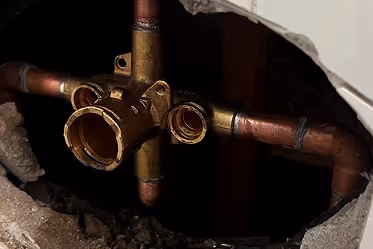 Close-up of copper plumbing pipes and a brass valve fitting within a wall cavity.