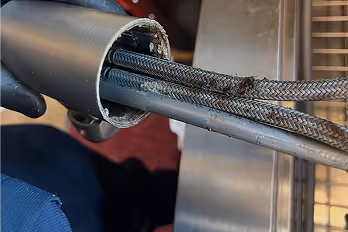 Gloved hand holding a partially cut flexible metal conduit with braided cables inside.