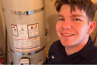 Young man smiling next to a grey water heater.