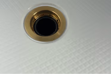 Close-up of a metallic gold-colored drain in a white textured surface.