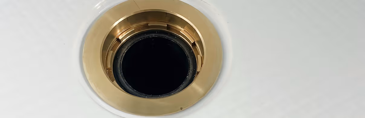 Close-up of a metallic gold-colored drain in a white textured surface.