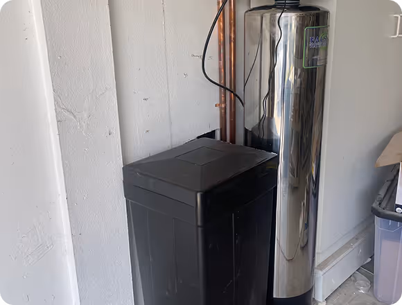 Water softener unit beside a tall stainless steel water filtration tank.