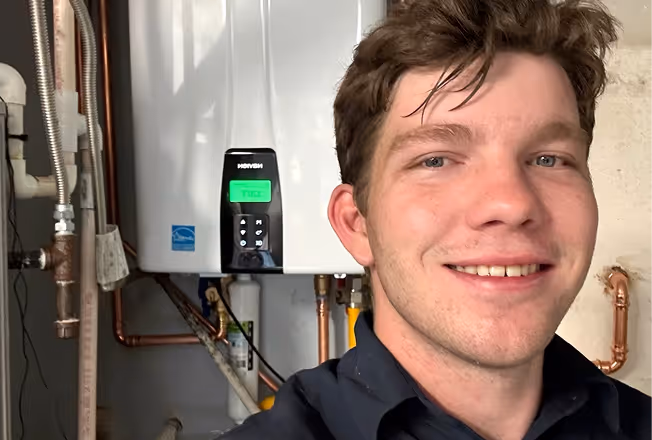 Smiling young man taking a selfie in front of a wall-mounted boiler.