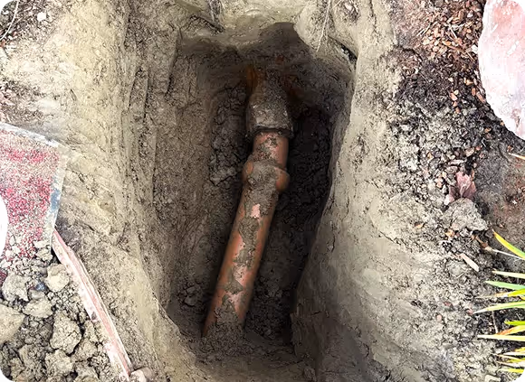 Excavated trench showing a partially buried pipe joint covered in dirt.