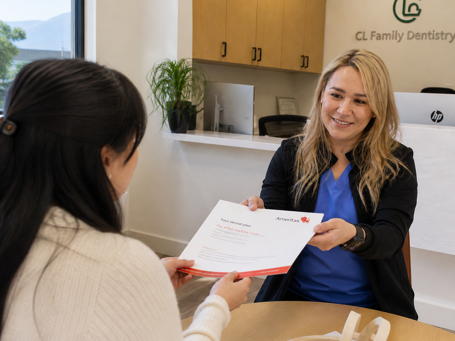 Office assistant smiling and handing an Ameritas insurance plan document to a seated patient across a desk in a bright, modern dental office reception area.
