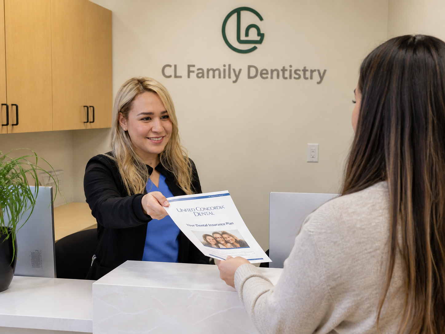 Friendly office assistant in a bright dental clinic reception area hands a United Concordia Dental insurance document to a patient across the front desk, captured in a natural, candid moment.