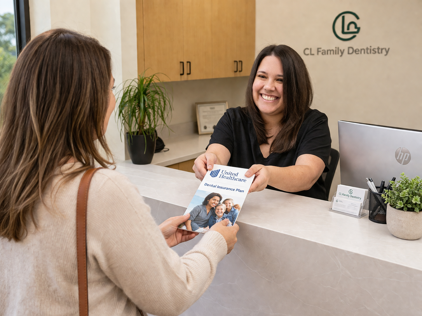 Friendly office assistant in a bright dental clinic reception area hands a UnitedHeathcare Dental insurance document to a patient across the front desk, captured in a natural, candid moment.