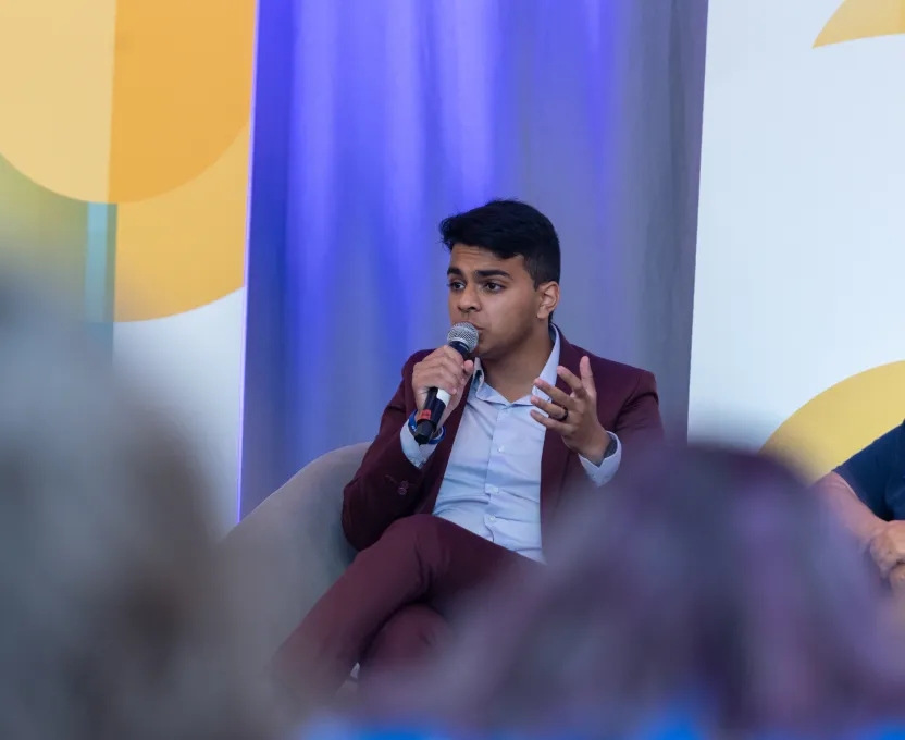 Man in a maroon suit speaking into a microphone during an event panel discussion.