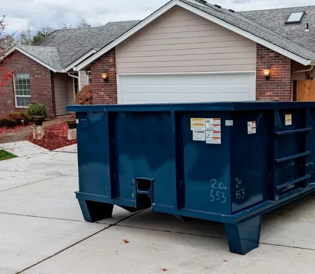 Large blue roll-off dumpster on driveway in front of a suburban house with brick and siding.