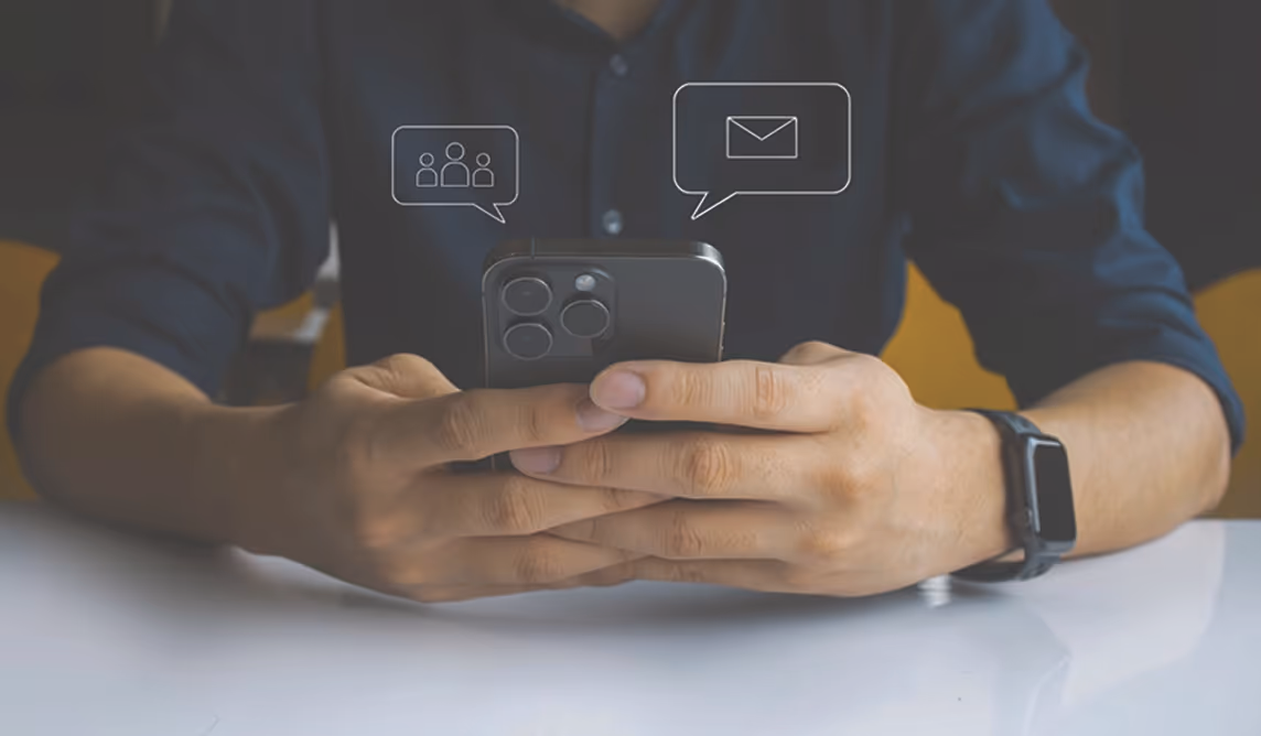 Чоловік у темній сорочці тримає смартфон із іконками повідомлень і групи над ним.