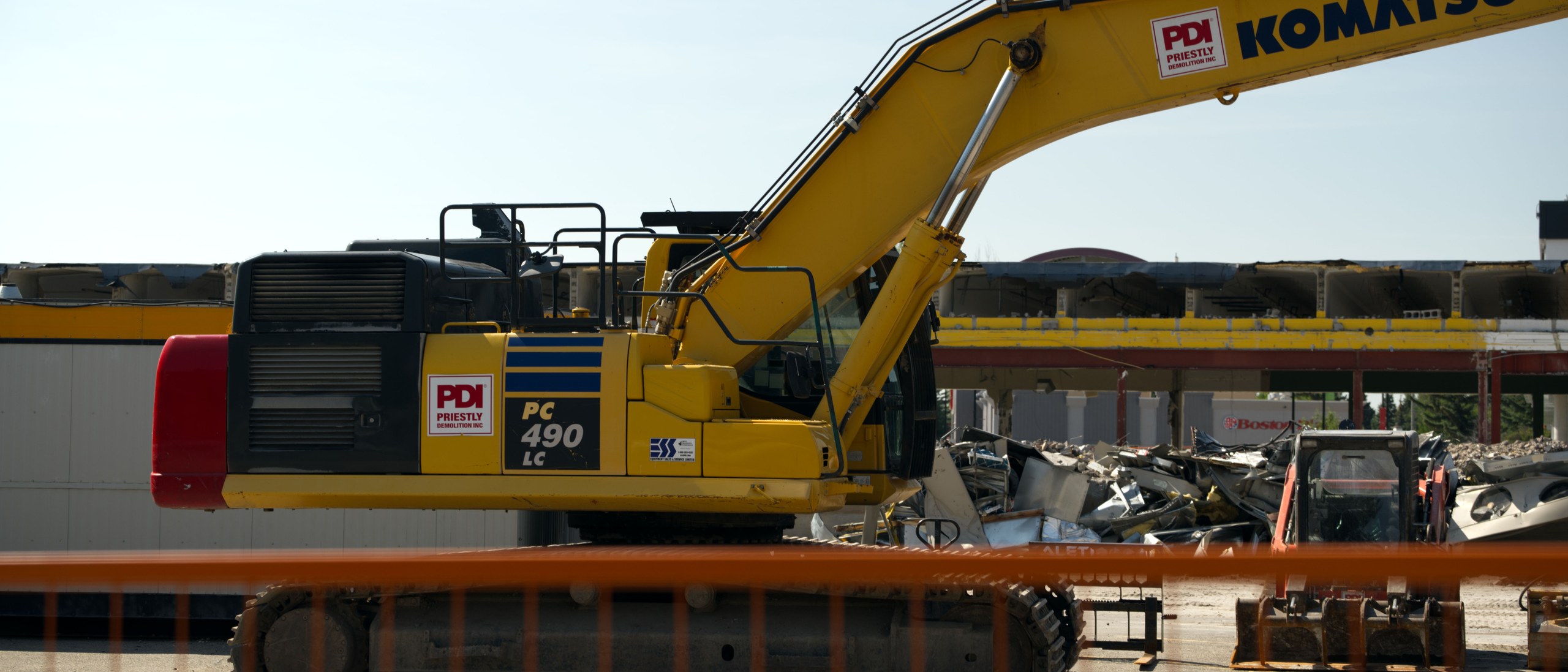 A Komatsu PC490 excavator working behind orange fencing at the Oakridge Co-op demolition in Calgary
