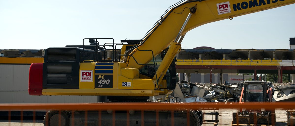 A Komatsu PC490 excavator working behind orange fencing at the Oakridge Co-op demolition in Calgary