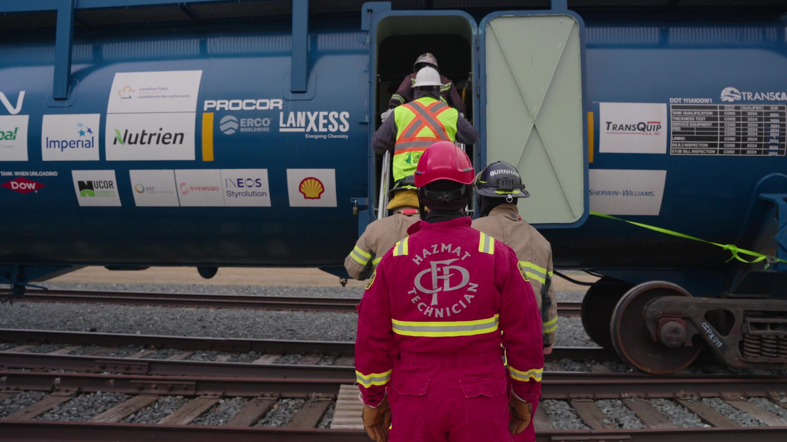 A HazMat technician in red coveralls approaching the manway of the CCPX 911 tank car