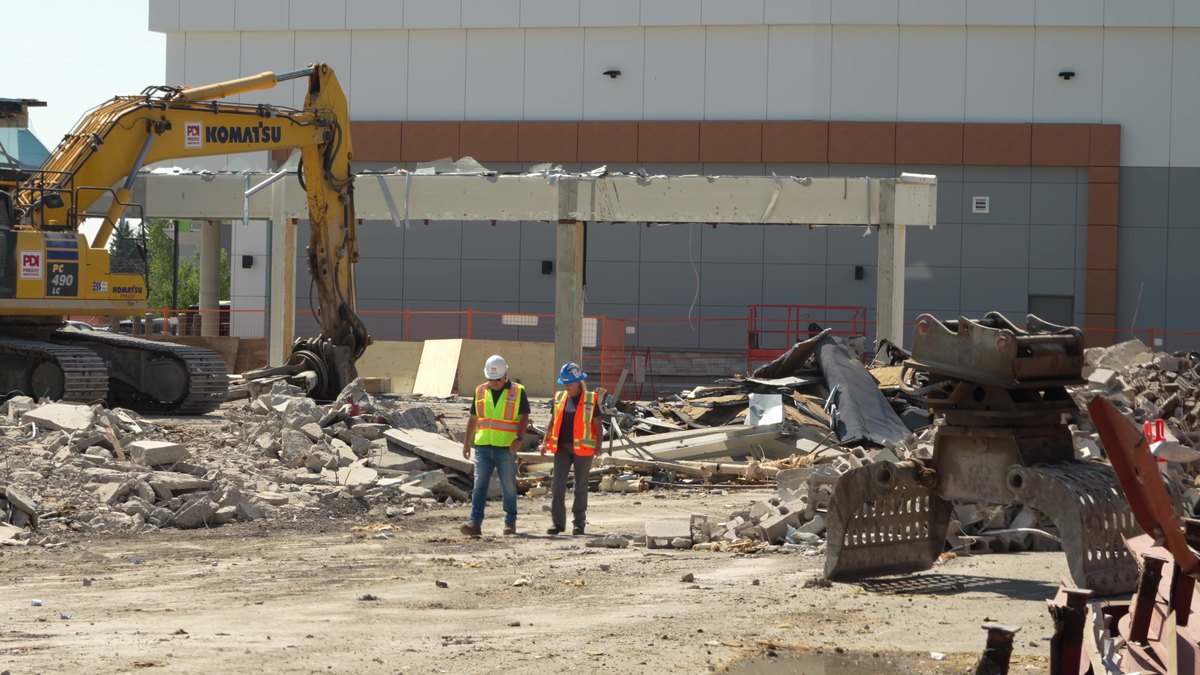 2 crew in hi-vis at the stripped Oakridge storefront beside a shear attachment