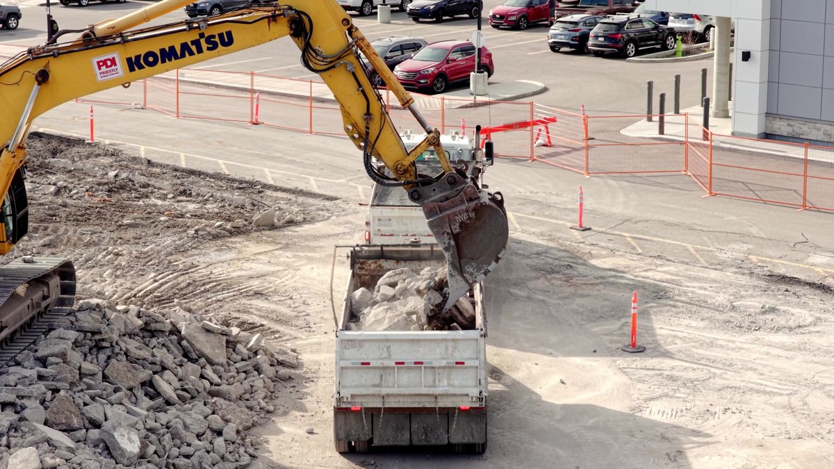 A Komatsu loading concrete rubble into a dump truck beside the live parking lot