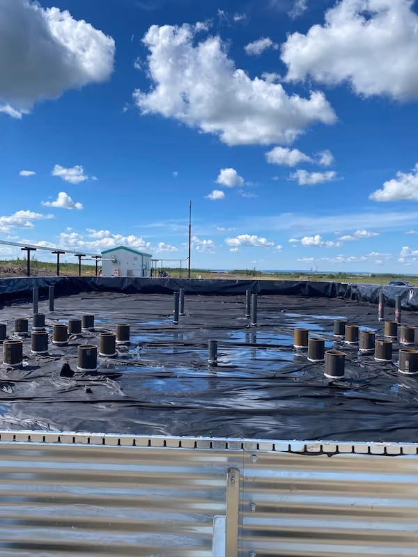 Large circular black lined containments with vertical pipes protruding under a blue sky with scattered clouds.