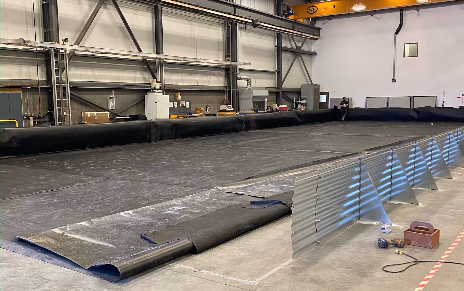 Large black containment liner spread out on a warehouse floor with metal barriers on one side.