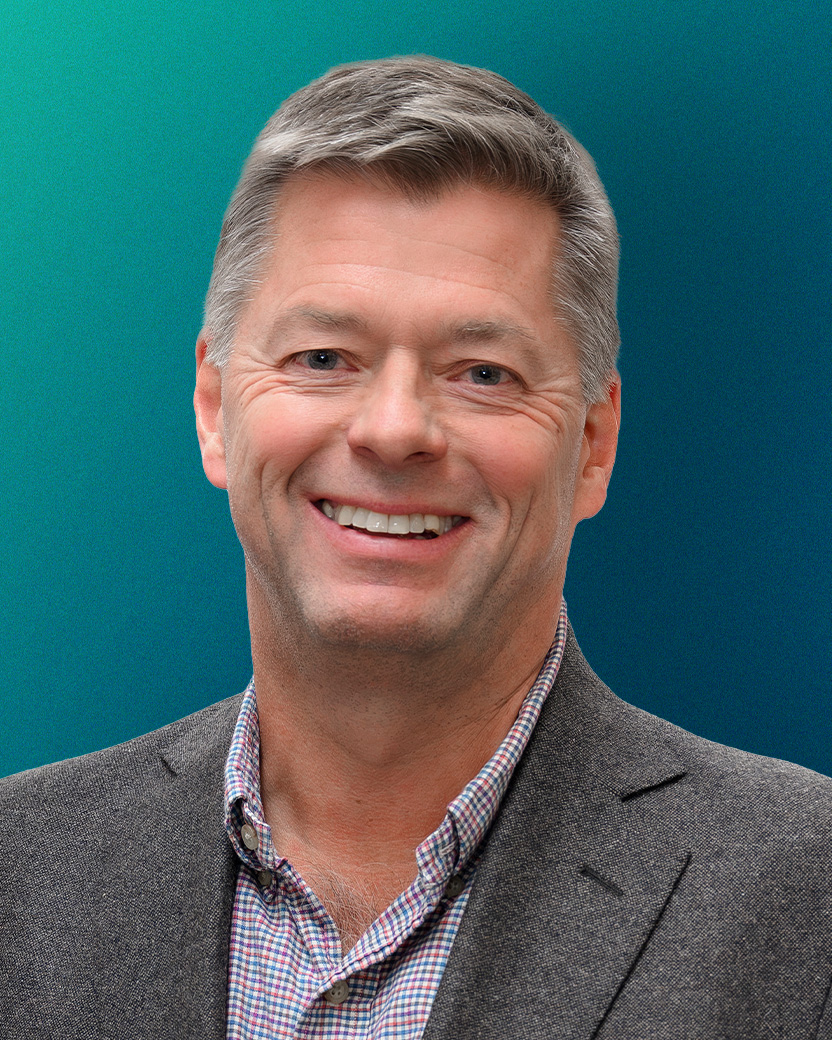 Smiling middle-aged man with gray hair wearing a checkered shirt and gray blazer against a blue-green gradient background.
