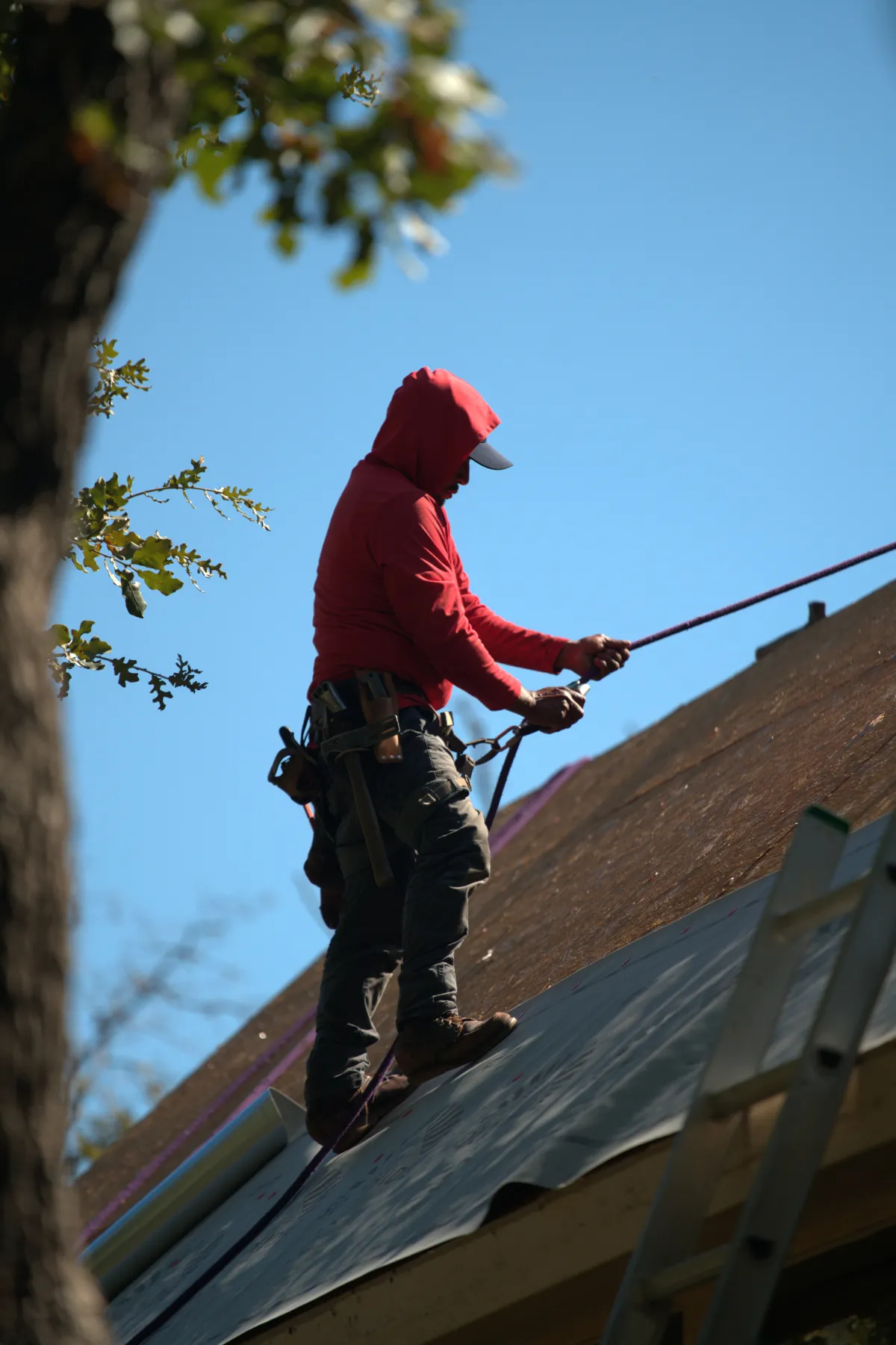 Roofer on a sloped roof holding on to the safety rope.