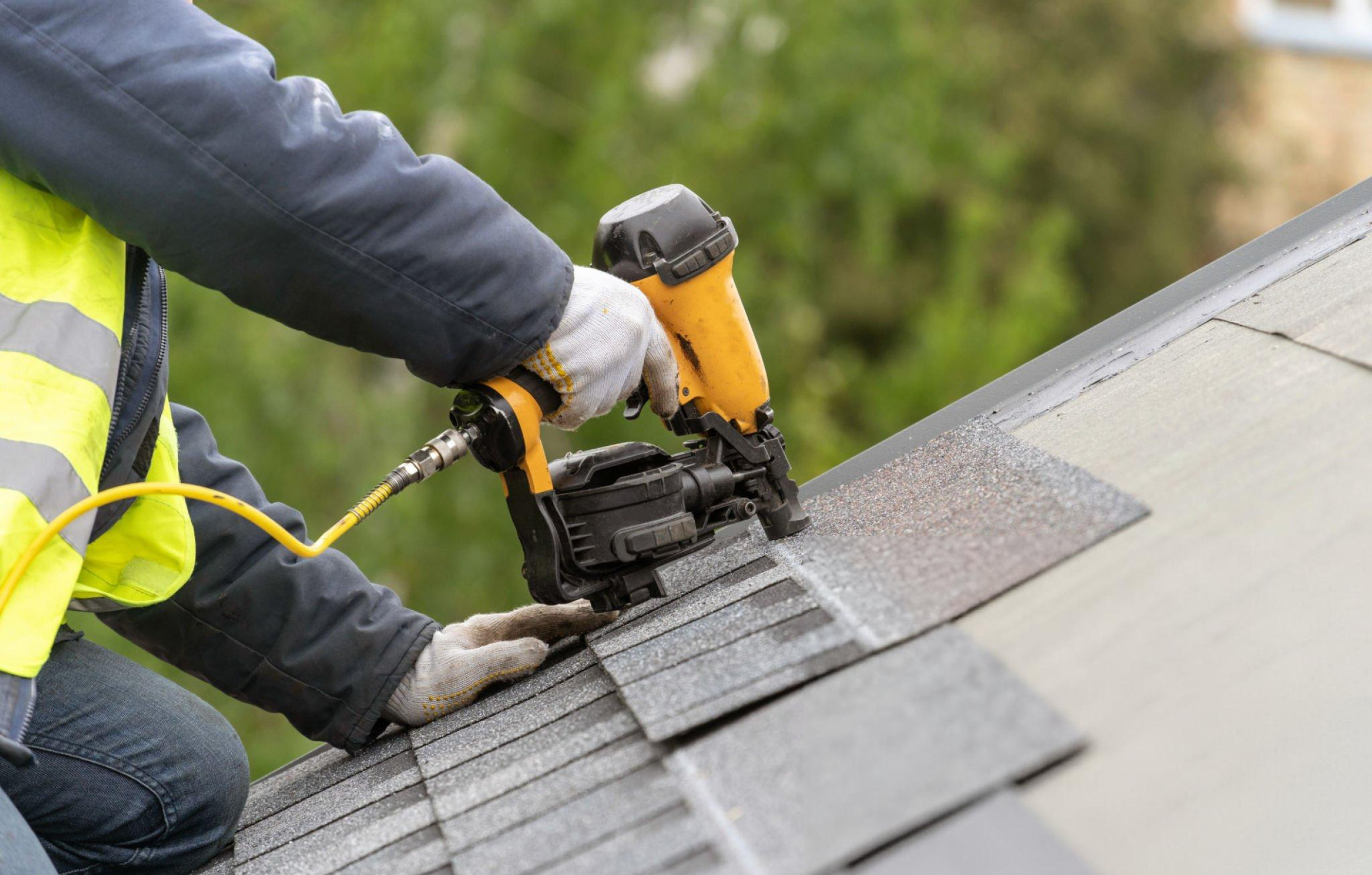 A guy on roof using a nail gun to repair shingles on a residential home.