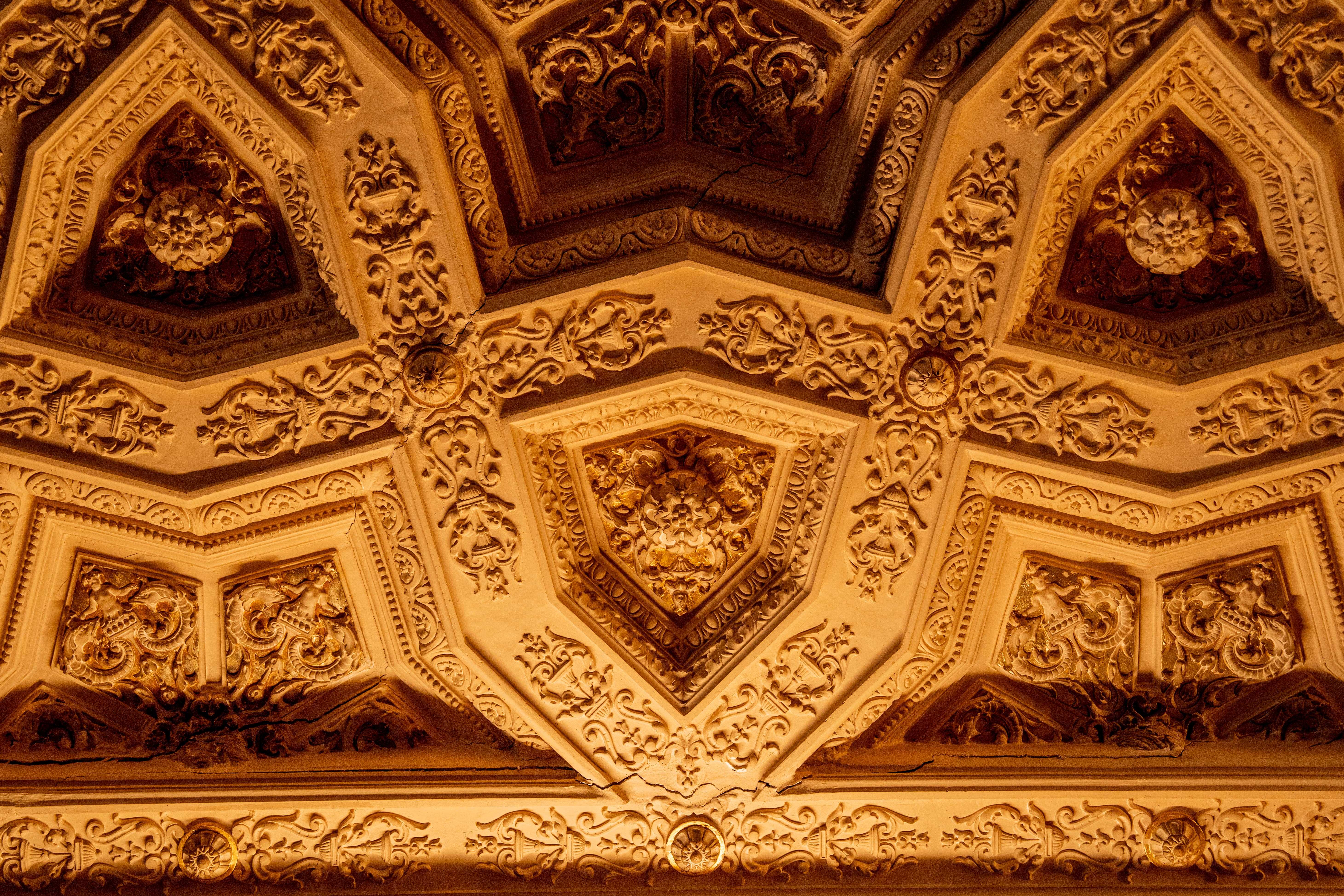 Ornate ceiling with intricate pentagonal and triangular relief carvings in warm tones.