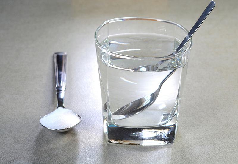 Spoonful of salt next to a glass of water