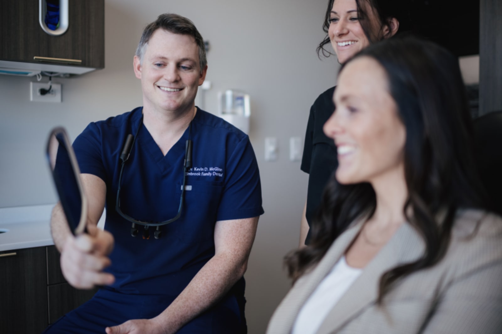 Elmbrook Family Dental team member in blue scrubs smiling with patients in modern dental office.