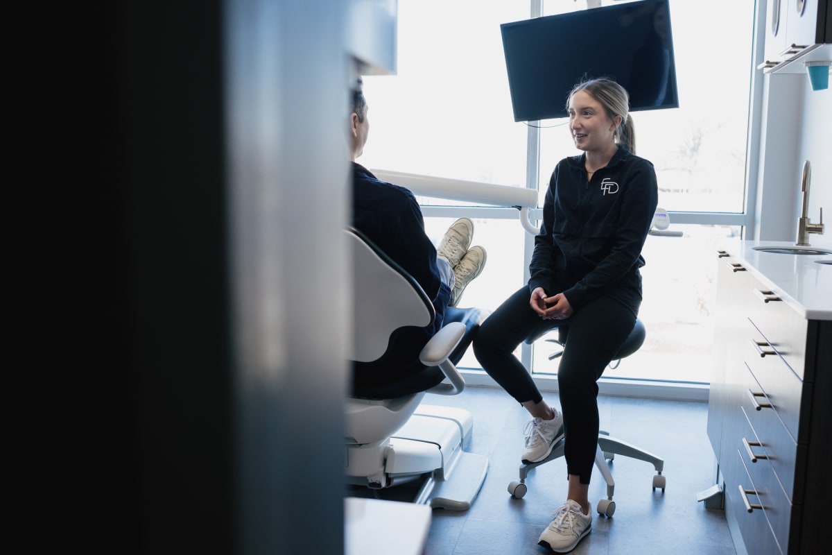 Female dentist in dark blazer discussing treatment with patient in modern dental office