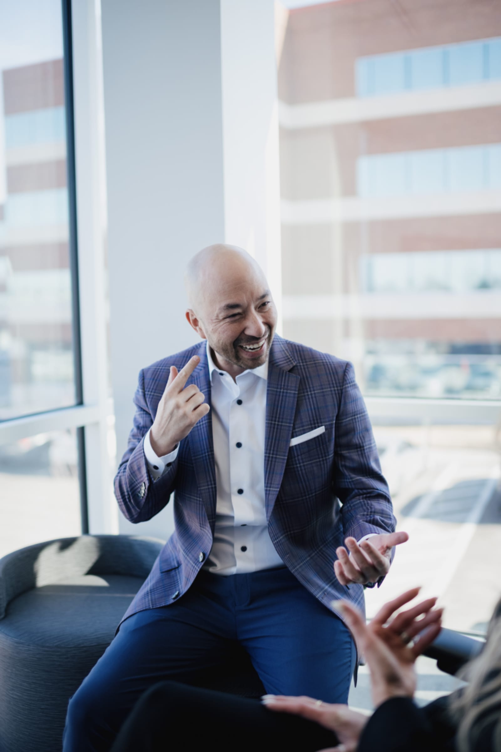 Male dentist in blue blazer sitting in modern dental office, gesturing while speaking.