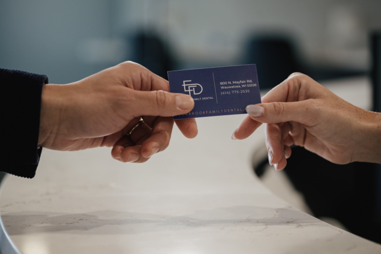 Two hands exchanging a blue business card across white surface