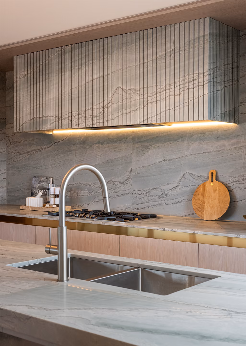 Modern kitchen with marble countertops, stainless steel faucet, and a stove with a wood cutting board.