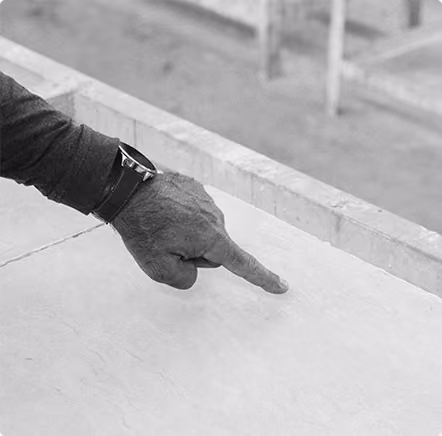 Person's hand with a watch pointing downward over a concrete surface.