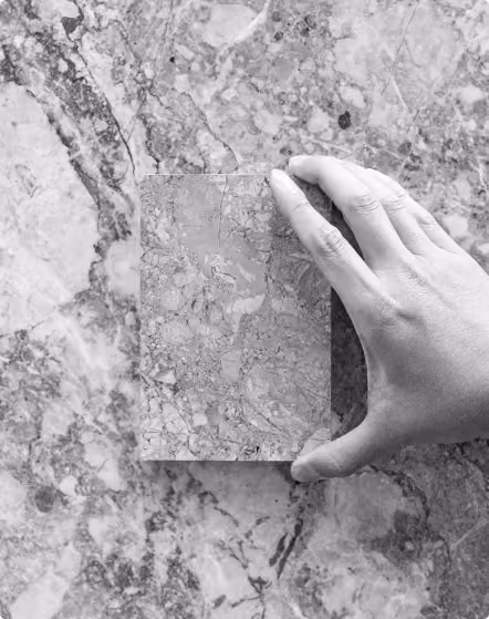 Hand holding a rectangular marble sample matching the marble surface beneath it.