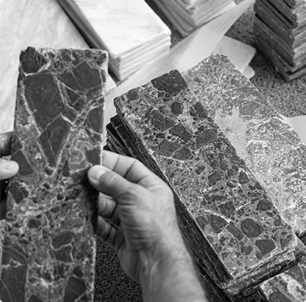 Hands holding and comparing marble tile samples with several stacked on a table.
