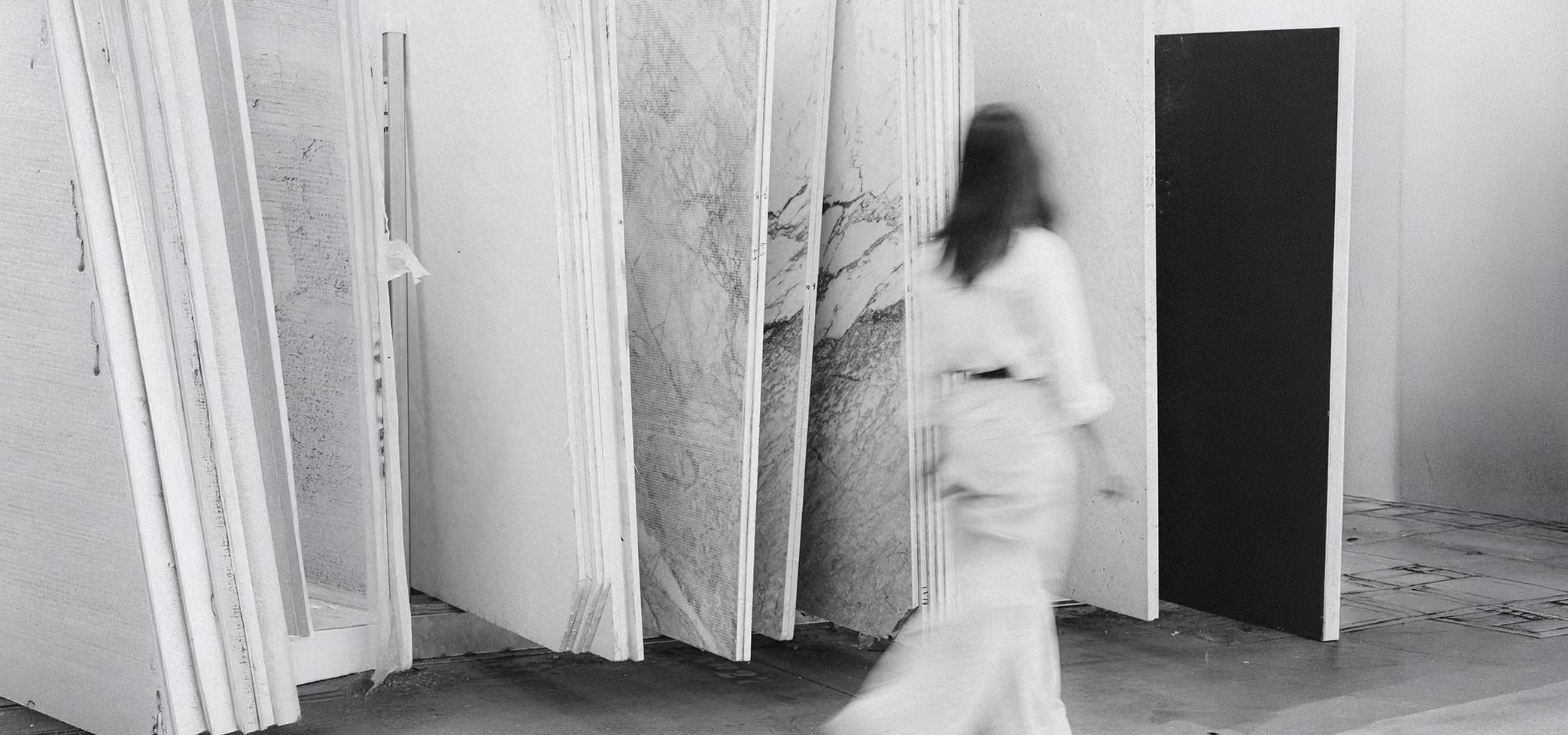 Blurred woman walking past large marble and stone slabs standing vertically in a showroom.