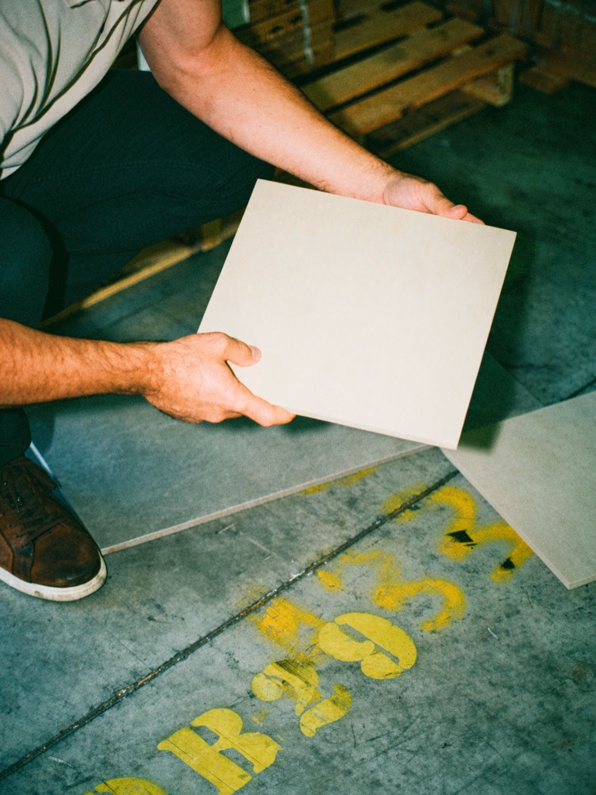Person holding a square beige tile above a concrete floor with yellow painted numbers.
