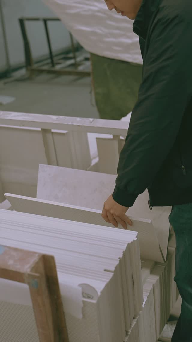 Person sorting or inspecting white ceramic or tile slabs stacked vertically in a workshop.