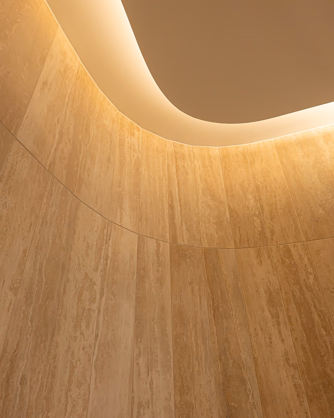 Curved beige stone wall with smooth ceiling and soft indirect lighting above.