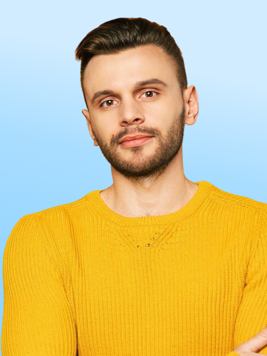 Man with a beard and short hair wearing a yellow sweater against a gradient blue background.