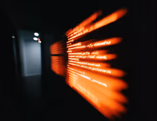 Blurred glowing orange programming code projected on a dark surface in a dimly lit room.