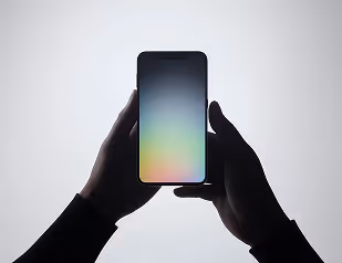 Silhouetted hands holding an illuminated smartphone with a gradient screen.