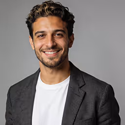 Smiling man with short dark hair and beard wearing a blue shirt.