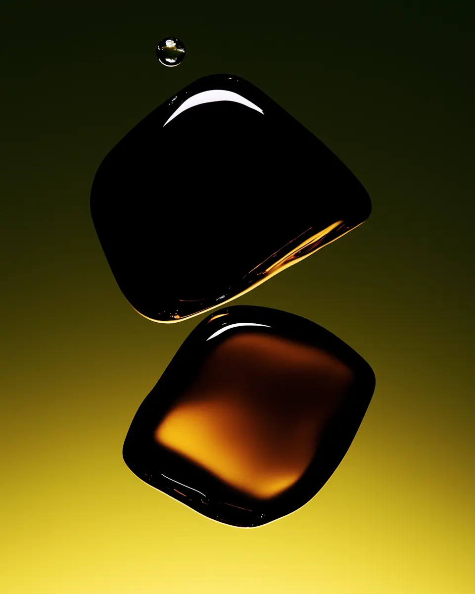 Two glossy, dark amber liquid shapes floating against a gradient yellow-green background.